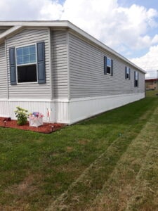 A gray mobile home with red mulch landscaping