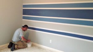 a man painting blue stripes on a wall