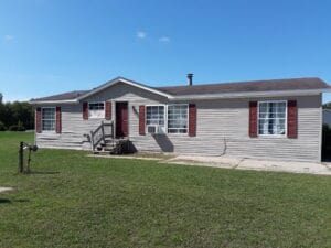 A gray doublewide manufactured home with burgundy shutters