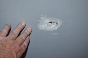A hole in the wall with a hand showing the damage