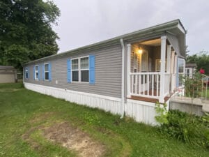 A gray doublewide with blue shutters and white deck