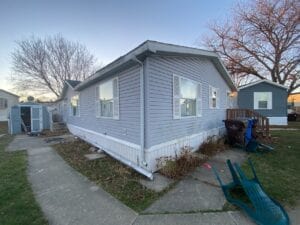 A gray mobile home with a sidewalk all around