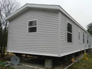 A gray singlewide mobile home that is on blocks