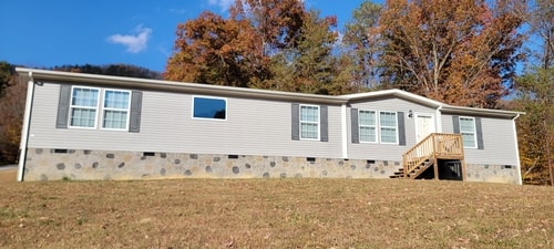 A gray doublewide with stone skirting