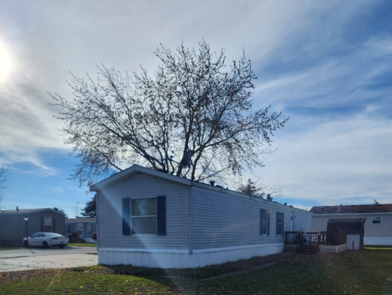 A gray singlewide with a blue sky above it