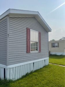 A gray singlewide mobile home with red shutters in a park