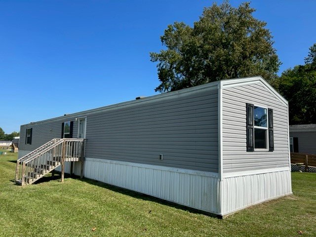 A singlewide mobile home on green grass with a small deck