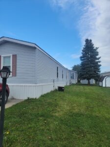 A gray singlewide with red shutters and green grass on the side