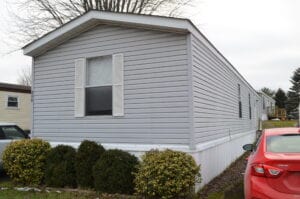 The front side of a gray singlewide with white shutters