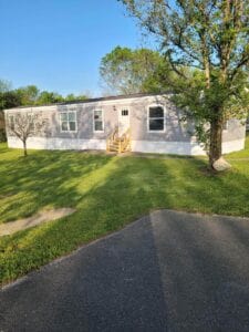 A large mobile home with white skirting and green grass