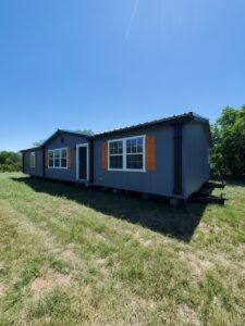 A dark gray mobile home with orange shutters