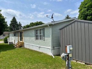 A green doublewide with a gray shed next to it