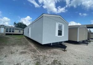 A gray mobile home with white shutters and a hitch on the front of it