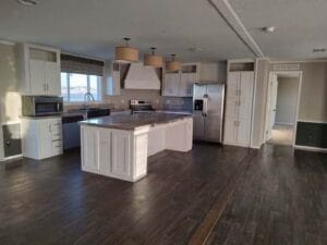 A mobile home kitchen with white cabinets and dark floor