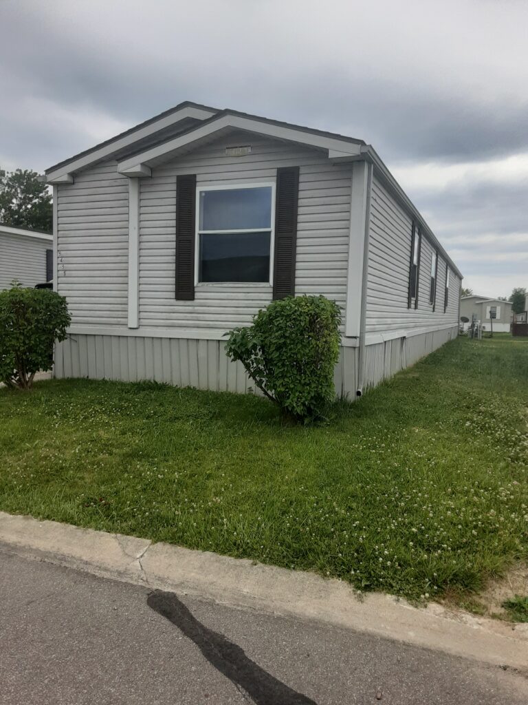 A newer gray singlewide mobile home with a shrub