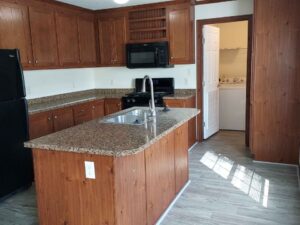 Kitchen on mobile home with dark wooden cabinets and granite counters, black appliances.