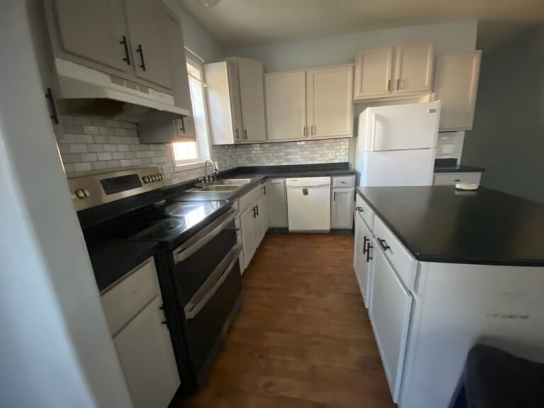 A kitchen in a mobile home with white cupboards and a dark wood floor