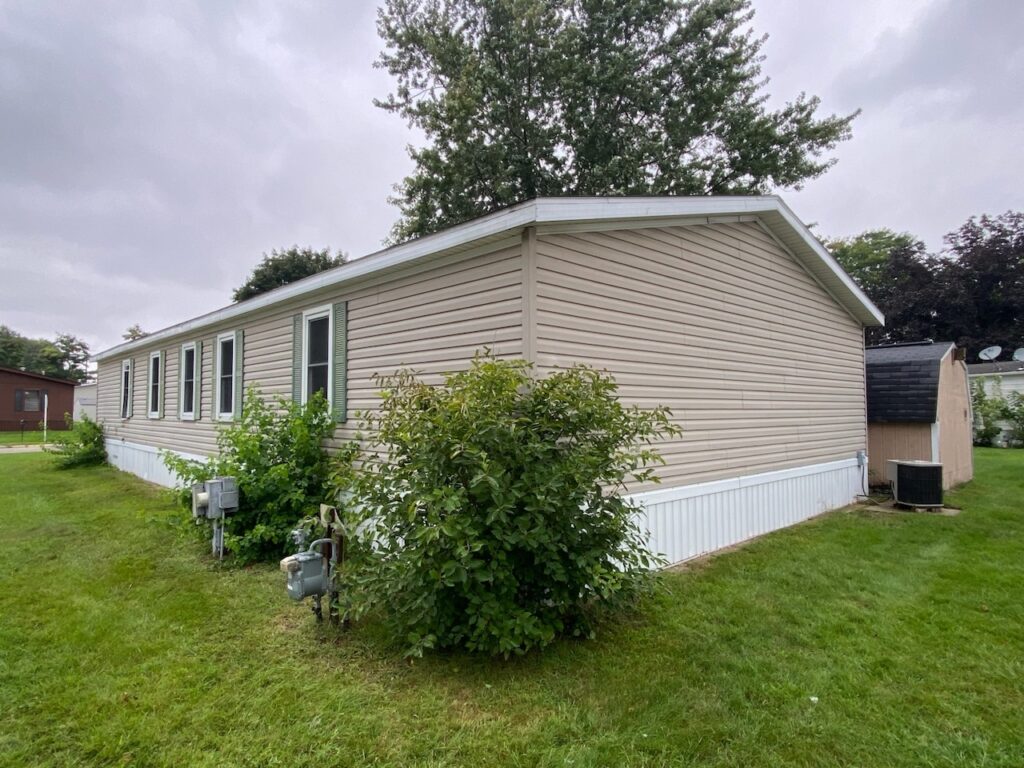 A brown doublewide with a large green bush on the side