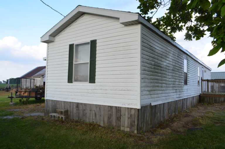 A white singlewide with dirty siding on it
