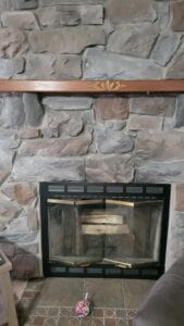 A stone fireplace with a black front and wood mantle
