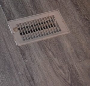 A mobile home floor vent in gray flooring