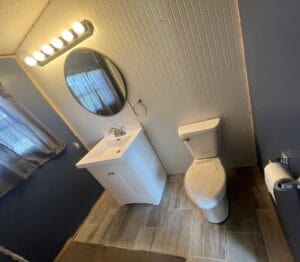 A small bathroom with a light bar mirror and toilet
