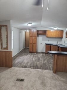 Inside of mobile home, wooden floor, wooden cabinets in kitchen area.