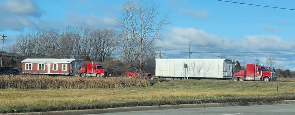 Two red toter trucks hauling a doublewide mobile home down the road