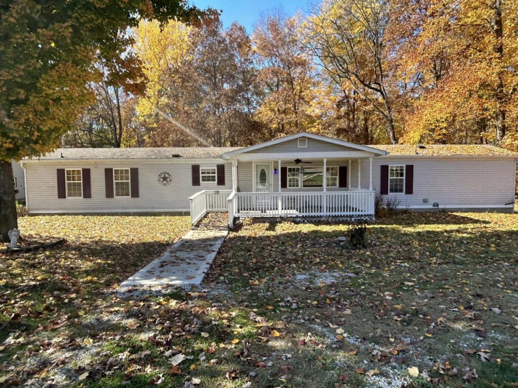 A doublewide with a covered porch and leaves all over the yard