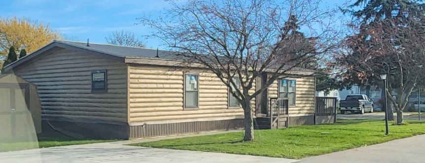 A log sided mobile home with dark brown roof and skirting