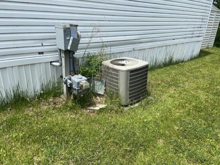 An outside air conditioner condenser with a bunch of weeds around it