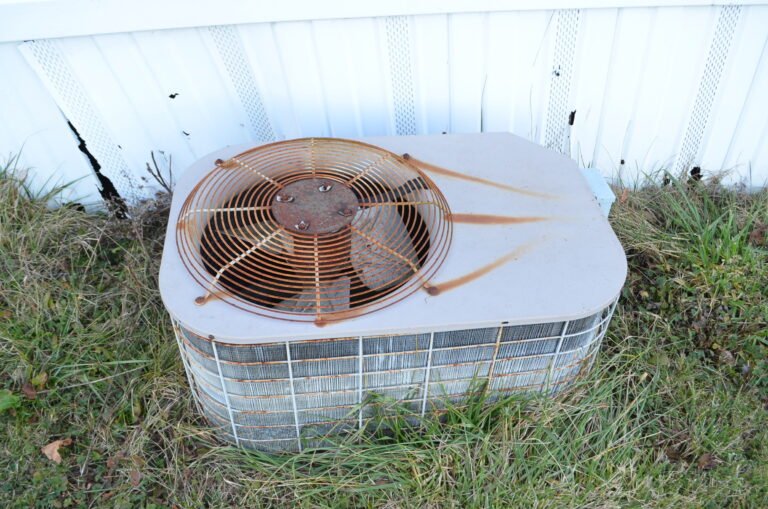 An air conditioning unit sitting in heavy grass that is rusted