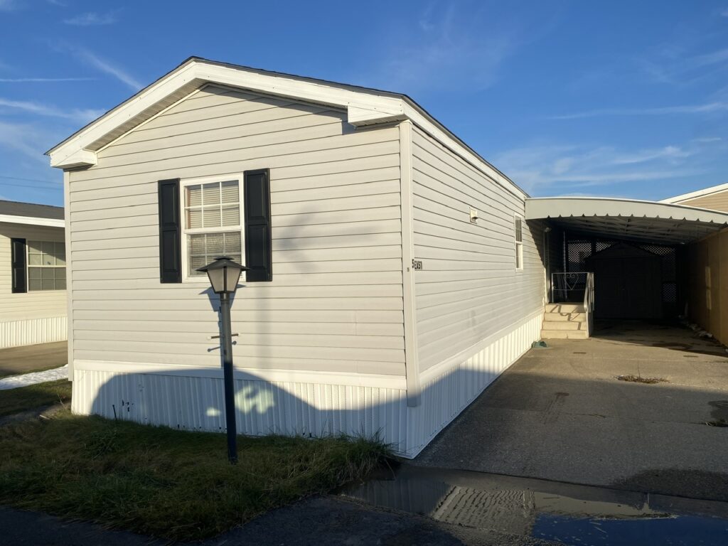 A gray sided singlewide with black shutters and white trim