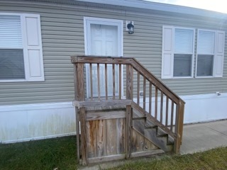 A tan colored doublewide with a small wood deck
