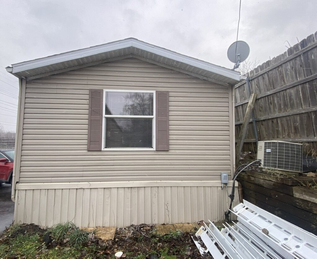 A tan colored singlewide with light brown shutters