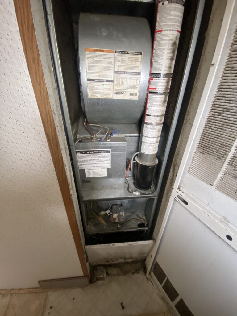 A furnace in a mobile home with the cover off from it