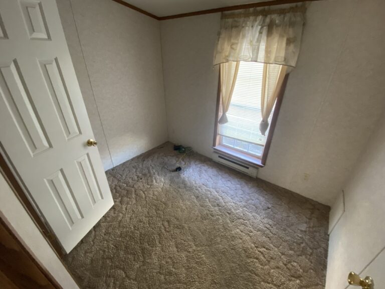 A small bedroom in a manufactured home with brown carpet