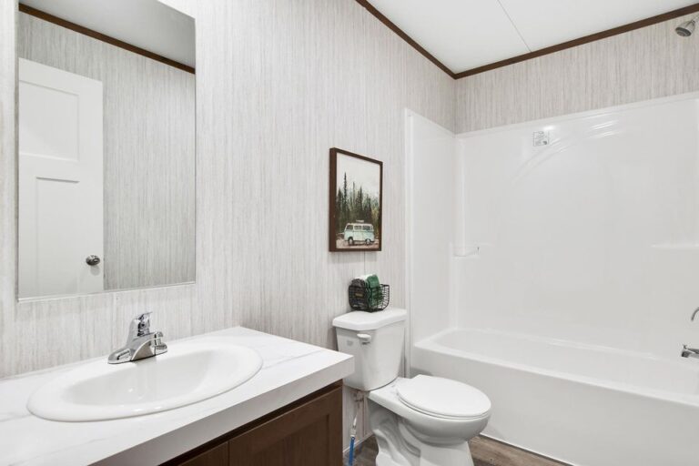 A white bathroom with brown cupboards and a picture over the toilet
