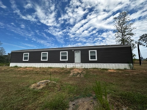 A dark gray singlewide mobile home on land