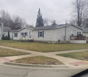 A gray doublewide mobile home with a large yard