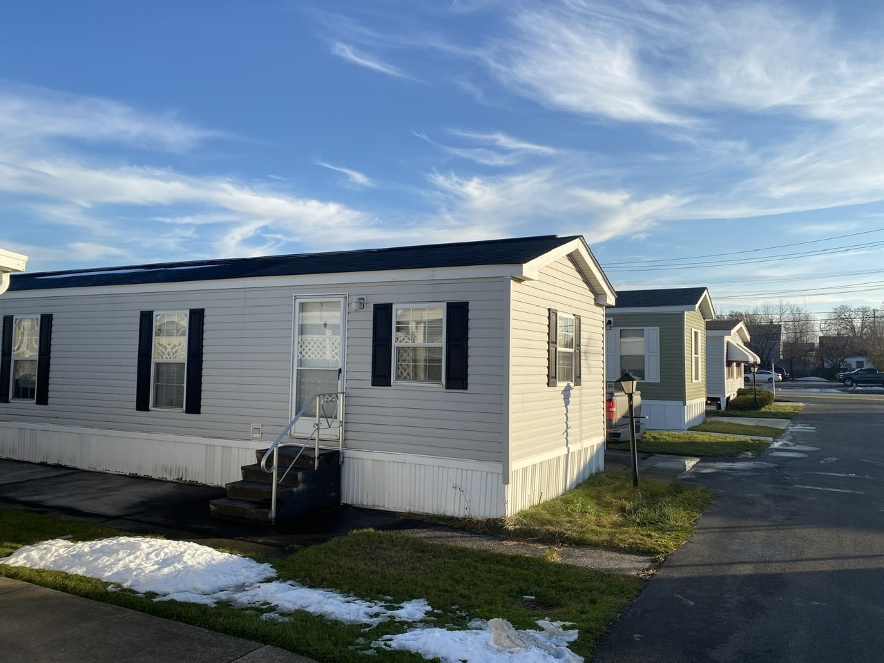 A gray singlewide mobile home with black roof