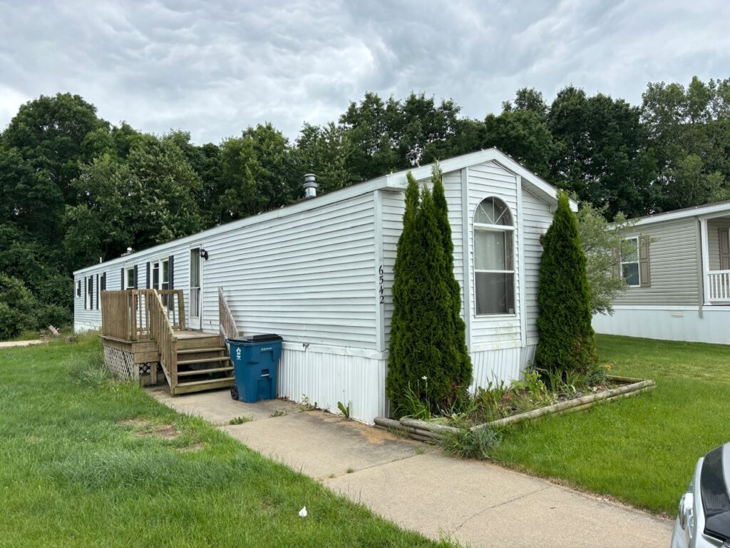 A white mobile home with tall pines next to it