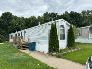 A white mobile home with tall pines next to it