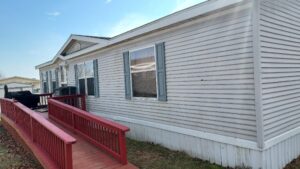 A doublewide with gray siding and a red deck