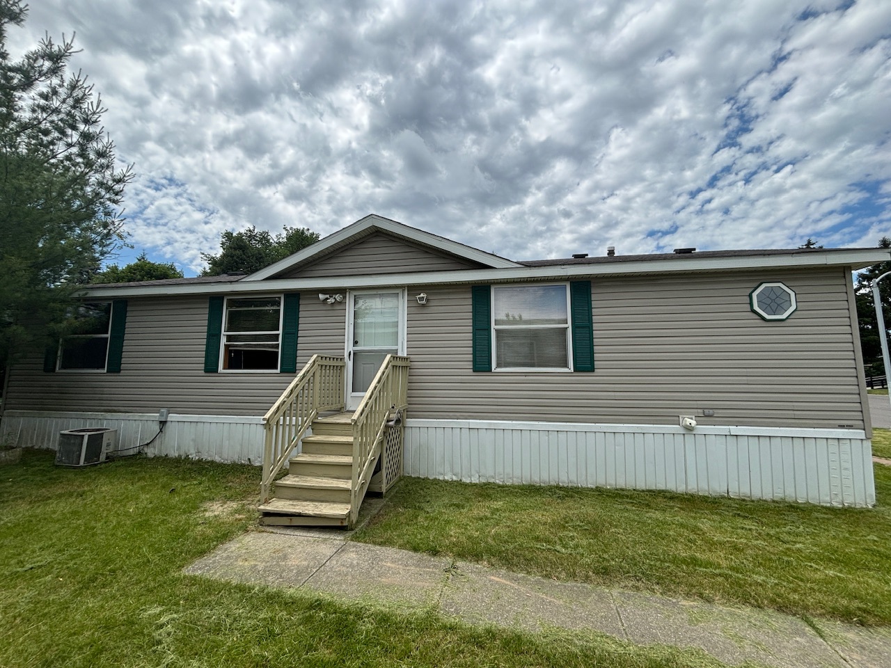 We Buy Mobile Homes - Quick Cash Sales Tan mobile home with green shutters and wooden steps sold for cash to experienced home buyers
